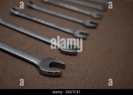 Combination wrenches with rings and open ends lined up on a wooden board in workshop. Selective focus on spanner fixed jaw Stock Photo