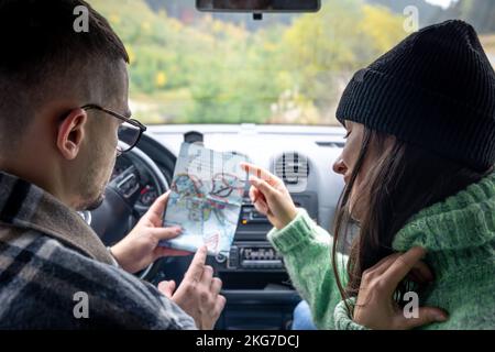A man and lady holding and looking at paper map, sitting inside car. Stock Photo