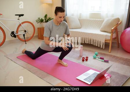 Woman following online fitness instrustor when doing deep lunges at home Stock Photo