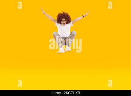 Funny crazy preteen boy having fun jumping high and hovering on orange background in studio. Stock Photo