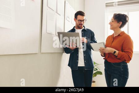Two happy business colleagues having a discussion while standing next to notice boards in an office. Two cheerful businesspeople planning a new projec Stock Photo