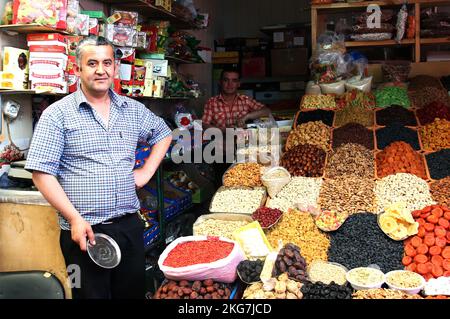 A male Vendor standing at Spices and Seasonings Green Bazaar. of dried fruits and nuts Stock Photo