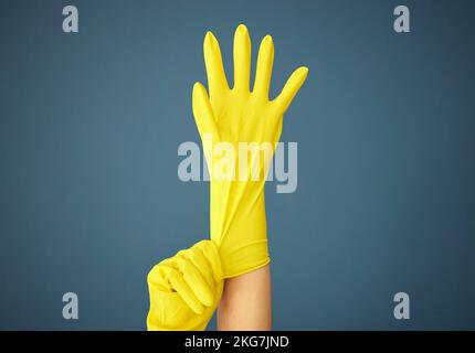 Cleaning, yellow rubber glove and hand on studio background for cleaner, hygiene and spring cleaning mockup on blue background. Hand of woman in Stock Photo
