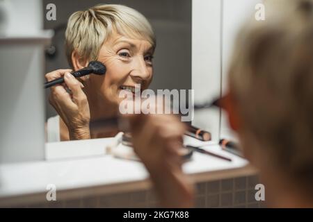 Mature woman is applying blush in the bathroom. Stock Photo