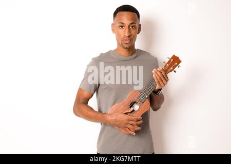 Young handsome african american man plays ukulele isolate over white background, Stock Photo