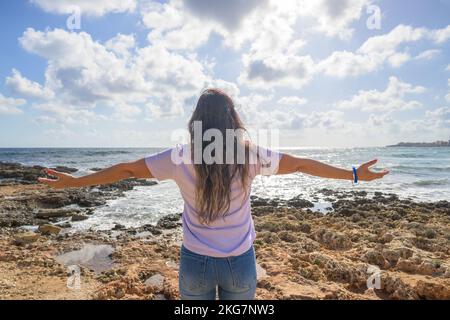 Middle-aged woman stretching her arms breathing fresh air on the Mediterranean coast in front of the sun. Stock Photo