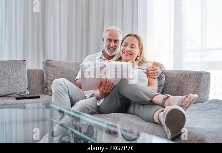 Senior couple reading book on sofa together enjoying weekend, freedom and retirement at home. Love, relaxation and mature man and woman read novel Stock Photo