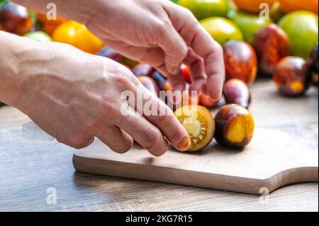 female hands put tomatoes on a chopping board on the table with different colored tomatoes, closeup Stock Photo