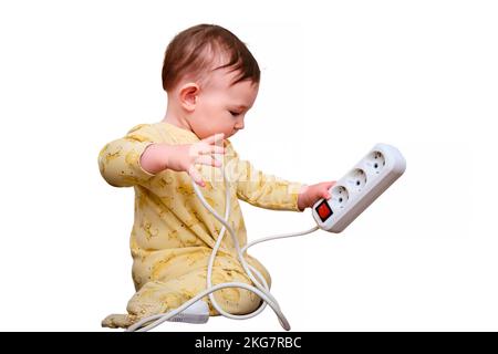 Toddler baby boy plays with electric wires while sitting on the floor, isolated on a white background. Child holding an extension cord with electrical Stock Photo