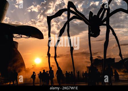 Sunset next to the Guggenheim Museum in Bilbao, a group of silhouettes walk near the sculpture Maman Stock Photo