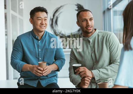 Smiling group of multiethnic colleagues drinking coffee and talking during break Stock Photo