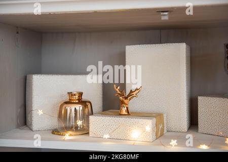 Behind the glass of a cupboard with dishes, shelves are decorated with Christmas toys, bright garlands, gifts in pink packaging. Toys in the shape of Stock Photo