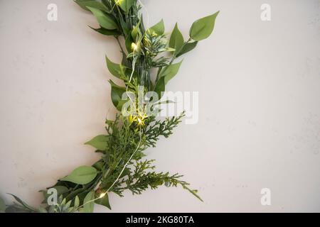 On gray concrete wall, there are three laconic, elegant, green wreaths made from natural materials. Festive garland. Minimalist interior decor in rust Stock Photo