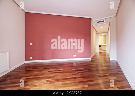Empty living room with reddish parquet flooring with a wine red painted wall and a hallway with wardrobes Stock Photo