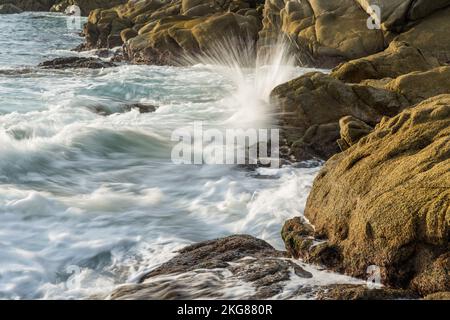 Waves crashing on the rocks on Chahue Beach in the Bahias of Huatulco, Mexico.  A slow shutter speed gives a silky look to the water. Stock Photo