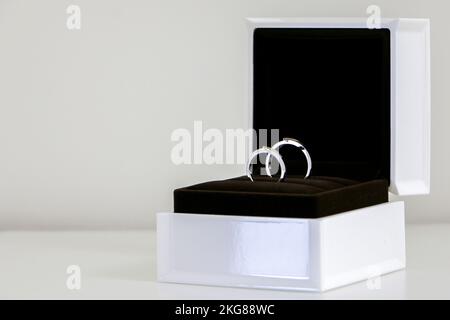 A couple of beautiful shiny wedding rings sparkling in open ring box on right side, isolated against white background, symbol of romance, love and mar Stock Photo