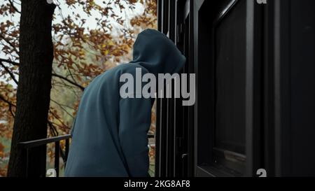 Thief in dark clothes picks door lock and enters house Stock Photo