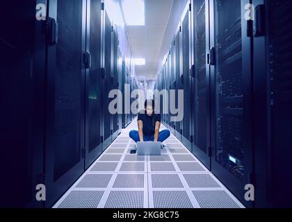 Female technician using laptop on floor in server room Stock Photo