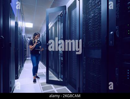 Female technician using smart phone and laptop in server room Stock Photo