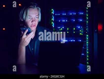 Technician using laptop and smart phone in server room Stock Photo