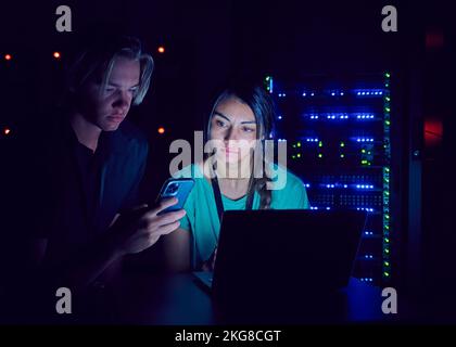 Technicians using laptop and smart phone in server room Stock Photo
