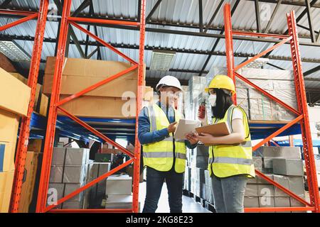 Two warehouse workers in white uniforms and yellow helmets on heads standing and talking about job Stock Photo