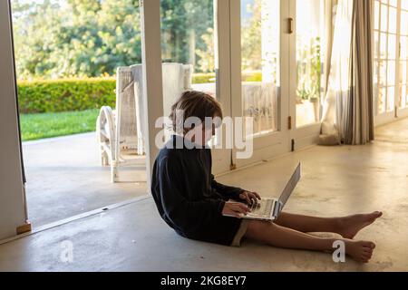 Boy (8-9) using laptop while sitting on floor Stock Photo