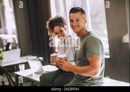 Cheerful coworkers with paper cups sitting on the office table Stock Photo