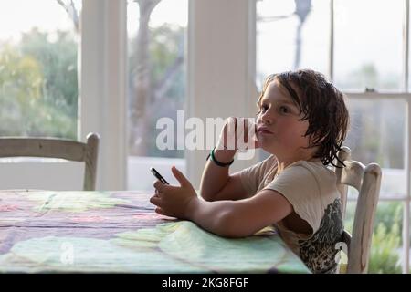 Boy (8-9) sitting at a table and using smart phone Stock Photo