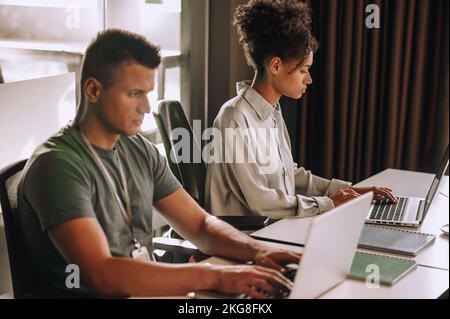 Two serious concentrated colleagues typing on their laptops Stock Photo