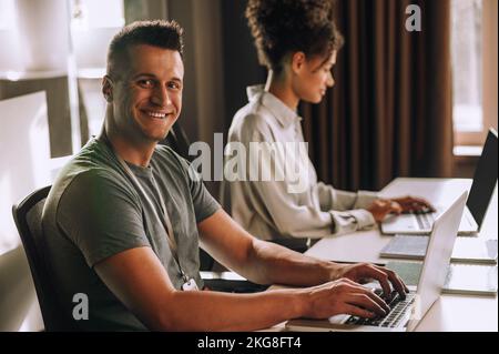 Cheerful office worker and his coworker working on portable computers Stock Photo