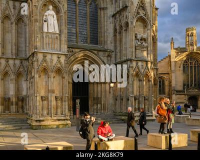 People taking selfies by new Elizabeth 2 statue on niche wearing Garter Robes (orb, sceptre) - York Minster west front, North Yorkshire, England, UK. Stock Photo