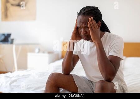 Depressed Young African American Man Sitting On Bed At Home Stock Photo