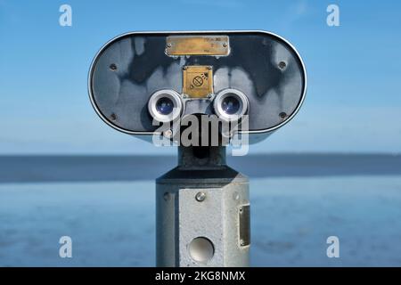 Old weathered retro stationary binoculars by the sea on a sunny day with blue sky. Stock Photo