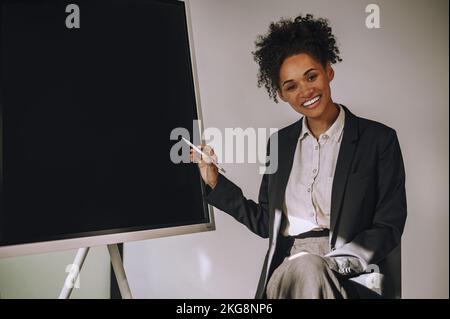 Joyful businesswoman pointing with a pencil at the board Stock Photo