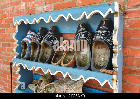 Old worn-out Dutch clogs or wooden shoes in a rack on a red brick wall Stock Photo