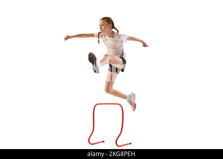 Dynamic portrait of little girl, professional athlete, runner, jogger at steeplechase training isolated over white background Stock Photo