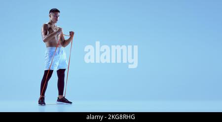 Portrait of young muscular man training with sports expander isolated over blue background in neon light. Flyer image Stock Photo