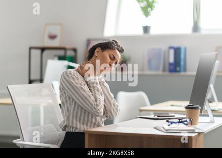 Neck pain. Exhausted young female entrepreneur massaging aching neck, suffering from ache, sitting in office Stock Photo