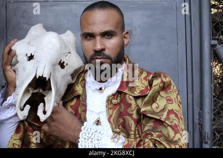 Ethnic man wearing baroque style outfit holding large skull Stock Photo