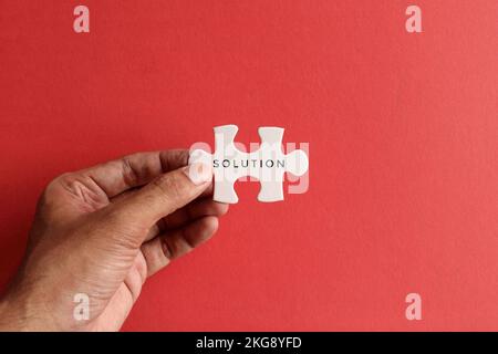 Hand holding puzzle pieces with text SOLUTION on red background. Top view with copy space Stock Photo