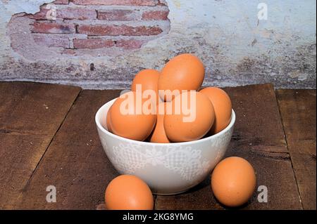 eggs in a bowl on a wooden table against a brick plastered wall Stock Photo