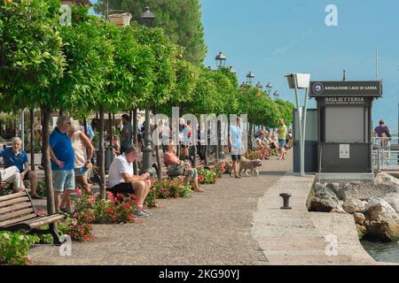 Gargnano Italy, view in summer of people relaxing beside orange trees lining the lakefront area in the scenic Lake Garda town of Gargnano, Lombardy Stock Photo