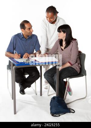 Teenagers: Working with Teacher. A pair of late teenage school pupils at a desk learning with their class tutor. From a series of related images. Stock Photo