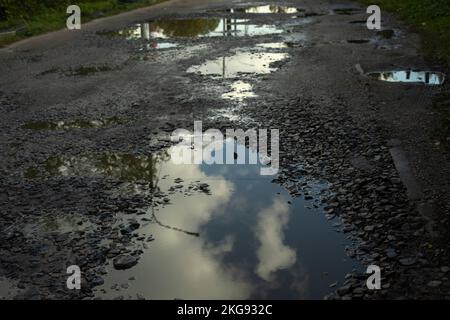 Large puddle on asphalt. Road with pits. Puddles on road. Rural highway details. Stock Photo