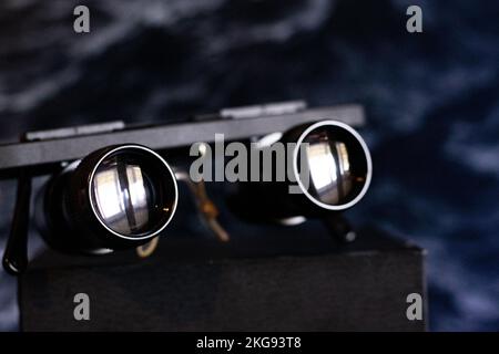 A closeup shot of black binocular glasses on a wooden surface in front of a dark background Stock Photo