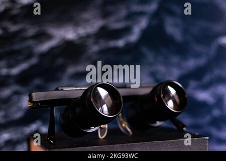 A closeup shot of black binocular glasses on a wooden surface in front of a dark background Stock Photo