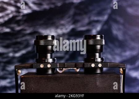 A closeup shot of black binocular glasses on a wooden surface in front of a dark background Stock Photo