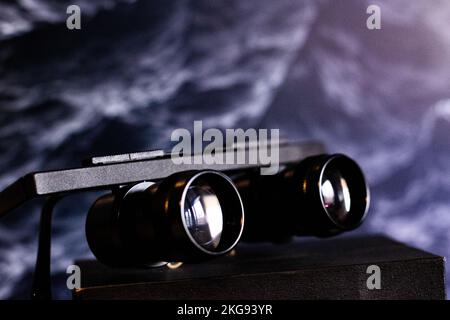 A closeup shot of black binocular glasses on a wooden surface in front of a dark background Stock Photo