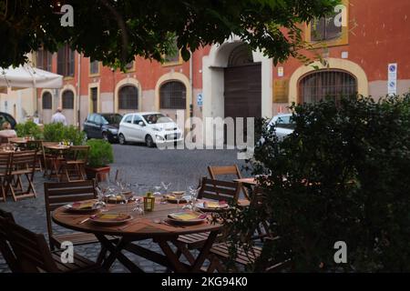 Cozy outdoor cafe table setting in the charming neighborhood of Trastevere. Al fresco restaurant dining setup along a cobblestone street in Rome, Italy. Stock Photo